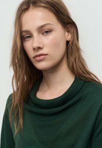 Un pull en maille vert avec un col drapé et une texture côtelée. Le design présente une silhouette ajustée et une finition douce.