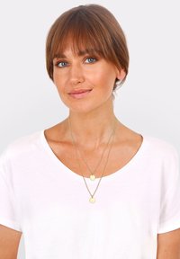 Guldtonede lagdelte halskæder med to cirkul�ære vedhæng. Kæderne er delikate og fine, og viser et simpelt, moderne design.