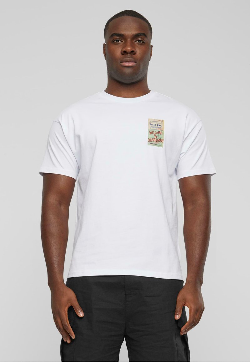 Hvid bomulds T-shirt med korte ærmer, der har et lille multifarvet grafisk mærke på venstre bryst, som viser tekst og designelementer.