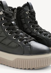 Baskets montantes noires avec un design matelassé, doublure en fausse fourrure et une semelle épaisse et texturée. Accents en métal et fermeture à lacets.
