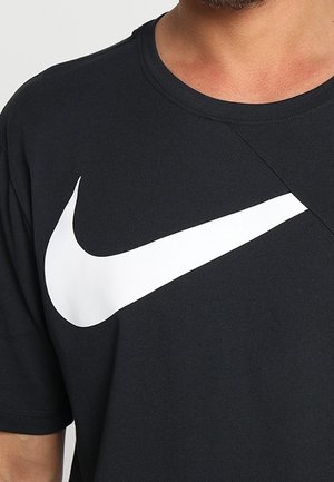Mężczyzna w czarnej koszulce z dużym białym logo Nike swoosh na piersi.