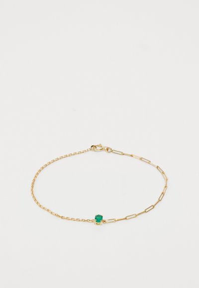 Bracelet en chaîne dorée présentant des maillons et une petite pierre verte, avec un fermoir à ressort. Design texturé avec des formes de maillons variées.