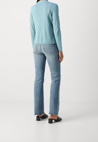 Pull léger bleu à manches longues, coupe ample, associé à un jean bleu clair avec un ourlet effiloché. Des mules à talons blocs noirs complètent la tenue.