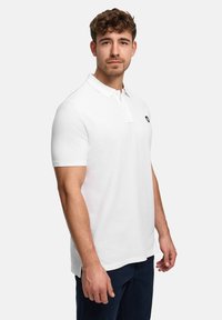 Hvid kortærmet poloshirt med klassisk krave og et lille logo på brystet. Stoffet virker tekstureret og åndbart.