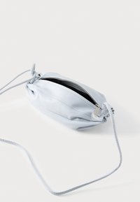 Τσάντα χιαστί από δέρμα ανοιχτού μπλε χρώματος με φερμουάρ στην κορυφή και λεπτό ρυθμιζόμενο λουρί σε λευκό φόντο.