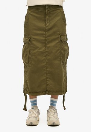 Jupe cargo verte olive avec poches latérales, fermeture à bouton et cordons de serrage réglables à l'ourlet. Portée avec des chaussettes rayées blanches et bleues et des baskets.