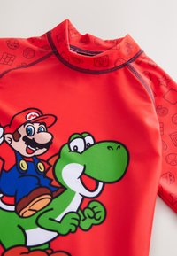 Red short-sleeve rash guard featuring Mario and Yoshi graphics, with a smooth texture and contrasting patterned collar.