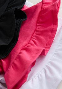 Kolme kangasharjaa mustana, vaaleanpunaisena ja valkoisena, jotka esittelevät sileitä tekstuureja ja poimuttuneita reunoja. Harjat on aseteltu päällekkäin.