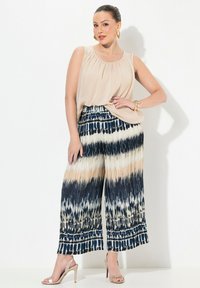 Beige ärmlös topp kombinerad med vida byxor i ett batikmönster i marinblått, kräm och beige. Prydd med en dekorativ midjeband.