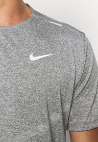 Camiseta atlética corta gris de manga corta hecha de tela texturizada. Presenta un logo de Nike blanco en el pecho y un cuello redondo con acentos mínimos.