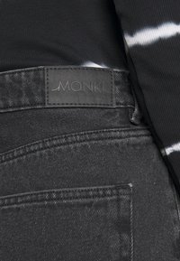 Mustat farkut ovat valmistettu teksturoidusta kankaasta, niissä on näkyvät saumat ja vyötärönauhassa on ommeltu etiketti, jossa lukee "MONKI."