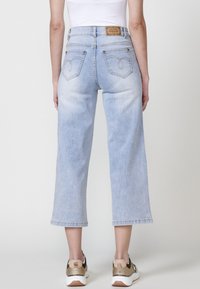 Jeans cortos de color azul claro con una textura ligeramente desgastada, que cuentan con dos bolsillos traseros y detalles de costura. Combinados con zapatillas oscuras.