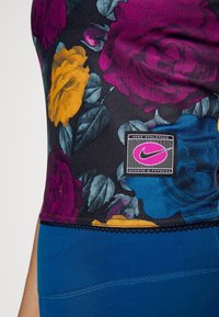 Květinový sportovní top s fialovými, žlutými a modrými růžemi na černém pozadí. Obsahuje černou značku Nike a modré sportovní šortky.