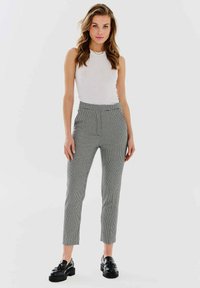 Szare spodnie w kratkę z wysokim stanem, dopasowanym krojem, zwężającymi się nogawkami i kieszeniami. Połączone z białą bluzką bez rękawów i czarnymi mokasynami.