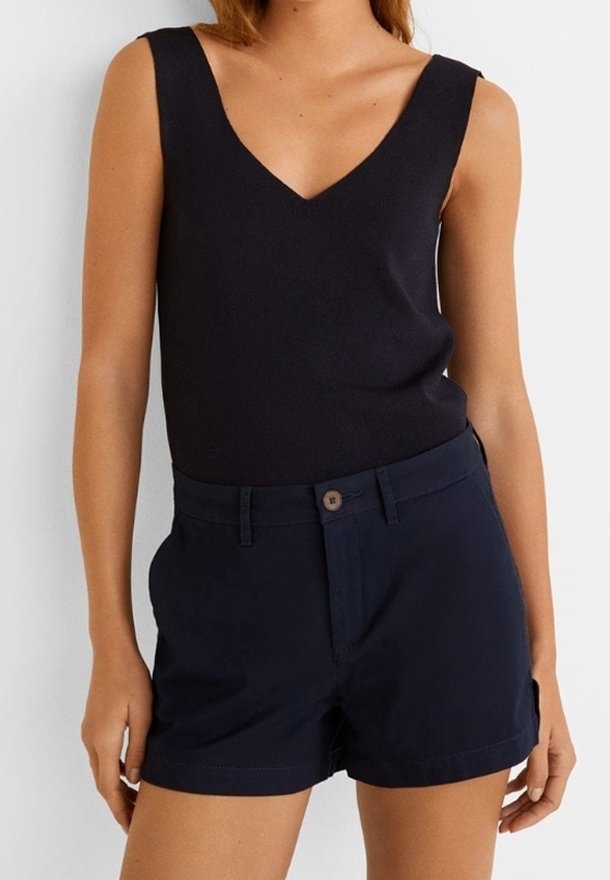Femme portant un haut noir sans manches à encolure en V et un short bleu marine taille haute avec un bouton et des passants pour ceinture.