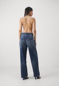 Bagest udsigt af en person iført en lys grøn halterneck top med krydsede stropper og bleget blå wide-leg jeans med baglommer.