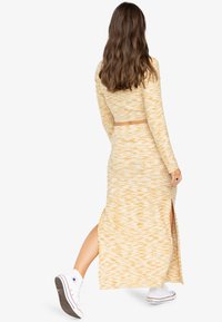 Un ensemble en tricot jaune à deux pièces comprenant un crop top à manches longues et une jupe longue avec des fentes latérales, associé à des baskets blanches.