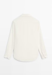 Bílá košile s dlouhým rukávem, klasickým límečkem, hladkou texturou, jemným leskem, zaobleným spodním lemem a manžetami na knoflíky. Pohled pouze zezadu.