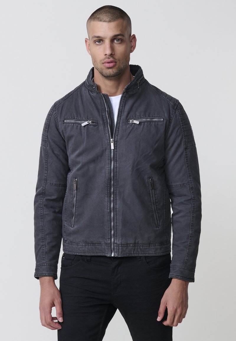 Férfi szürke farmerdzseki két cipzáras mellzsebbel, oldalsó zsebekkel és álló gallérral. Varrott részletezés a vállakon és az ujjakon.