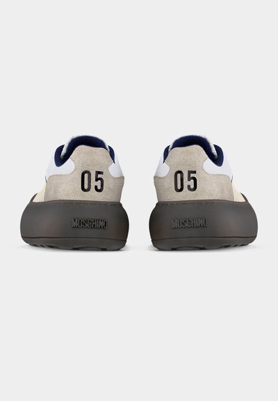Ζευγάρι μπεζ και λευκά αθλητικά παπούτσια με σκούρες σόλες, πίσω όψη, με αριθμό "05" και ανάγλυφο λογότυπο "MOSCHINO" στη φτέρνα.