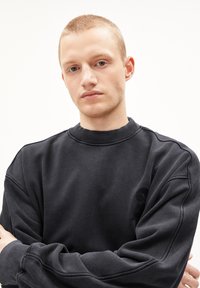 Black sweatshirt with a crew neckline, ribbed cuffs, and a textured print on the left chest area. Soft material with a relaxed fit.