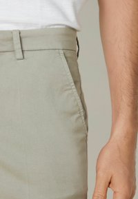 Ljust grå bomullsbyxor med rak skärning, sidofickor och ren sömnadsdetaljering. Tyget ser slätt och något matt ut.