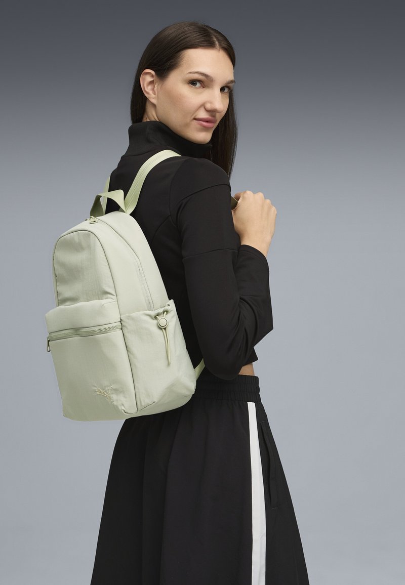 Sac à dos vert clair en matériau doux, avec une poche zippée à l'avant, des bretelles réglables et un design arrondi.