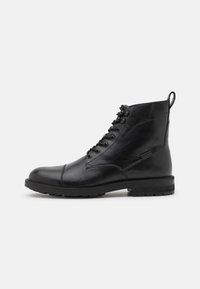 Bottine noire en cuir à lacets avec bout renforcé, semelle robuste et languette à l'arrière, vue de profil sur un fond uni.