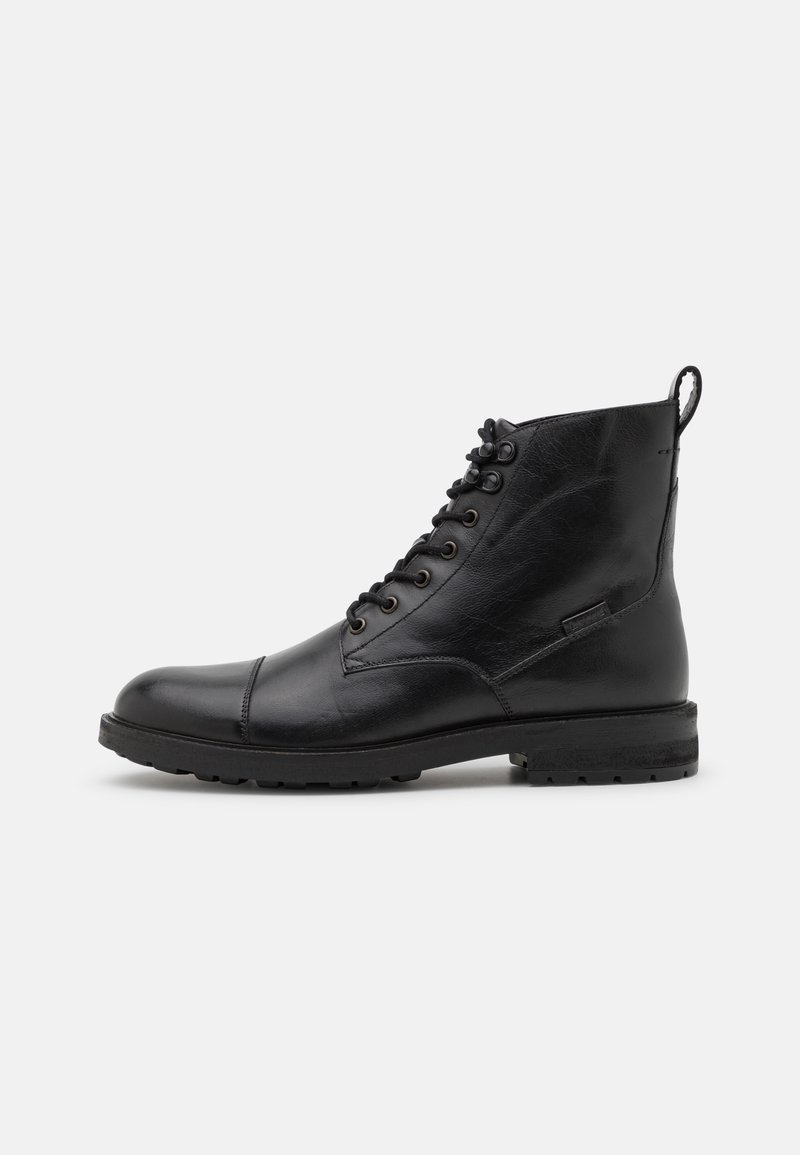 Bottine noire en cuir à lacets avec bout renforcé, semelle robuste et languette à l'arrière, vue de profil sur un fond uni.
