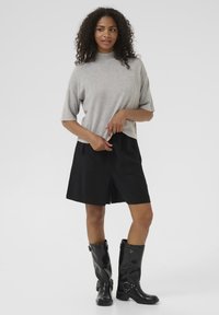 Top grigio chiaro a maniche corte con collo alto, abbinato a pantaloni corti neri con due tasche frontali e stivali neri in pelle al ginocchio.