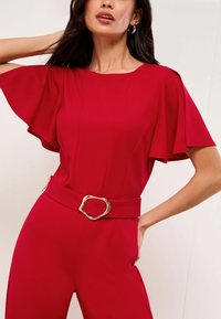 Rode jumpsuit met wijd uitlopende mouwen, een gladde textuur en een brede riem met een gouden ovale gesp. De strakke pasvorm benadrukt de taille.