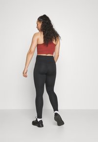 Svarte høy midje leggings kombinert med en rød kort topp. Leggingsene har tettsittende passform med en jevn tekstur. Svarte treningssko fullfører antrekket.