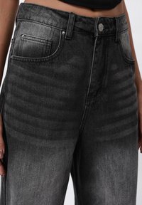Sorte denimjeans med en falmet tekstur, foran og baklommer, og en knappelukking, som viser en blanding av mørke og lyse grå nyanser.