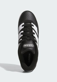 Svart och vit träningssko med en perforerad svart läderöverdel, tre vita ränder, svarta snören och en vadderad krage.