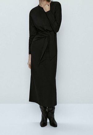 Robe midi noire à manches longues, corsage ajusté et ceinture nouée à la taille. Tissu lisse avec un design simple et une silhouette droite.