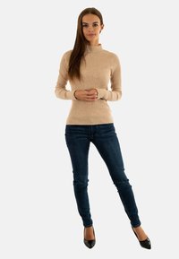Maglione beige a coste con collo alto, design aderente e maniche lunghe, abbinato a jeans slim-fit blu scuro e décolleté nere a punta.