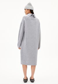 Grijze oversized jurk met lange mouwen, een kraag en een rechte silhoutte. Gepaard met een geribde grijzebonie en zwarte versierde schoenen.