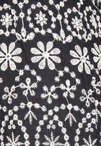 Zwarte stof met witte bloemenborduurwerk, met grote en kleine bloemen die verbonden zijn door delicate stelen en lussen.