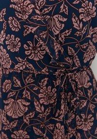 Tissu bleu marine avec motif floral rose poudré, avec des feuilles et des fleurs, noué à la taille avec une ceinture assortie.