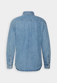 Camicia in denim azzurro chiaro con maniche lunghe, polsini abbottonati, colletto classico e una piega sul retro. Presenta un orlo curvo e cuciture robuste.