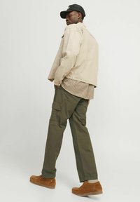 Beige corduroyjakke over en ternet skjorte, parret med olivengrønne cargo-bukser og brune ruskindssko. En sort kasket fuldender outfittet.