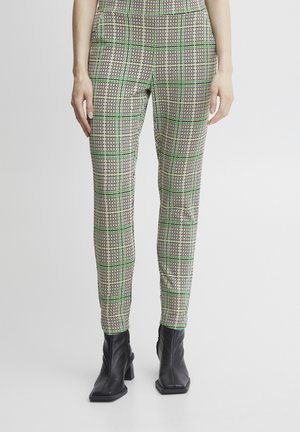 Fitted trousers in a beige, green, and black checkered pattern. Material appears smooth with a slight sheen. Worn with black ankle boots.