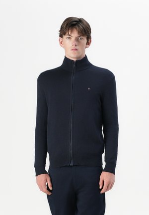 Tume sinine zip-up sviiter kõrge kaelusega, soonikute ja äärtega. Valmistatud pehmest kangast, millel on rindkere küljes väike logo.