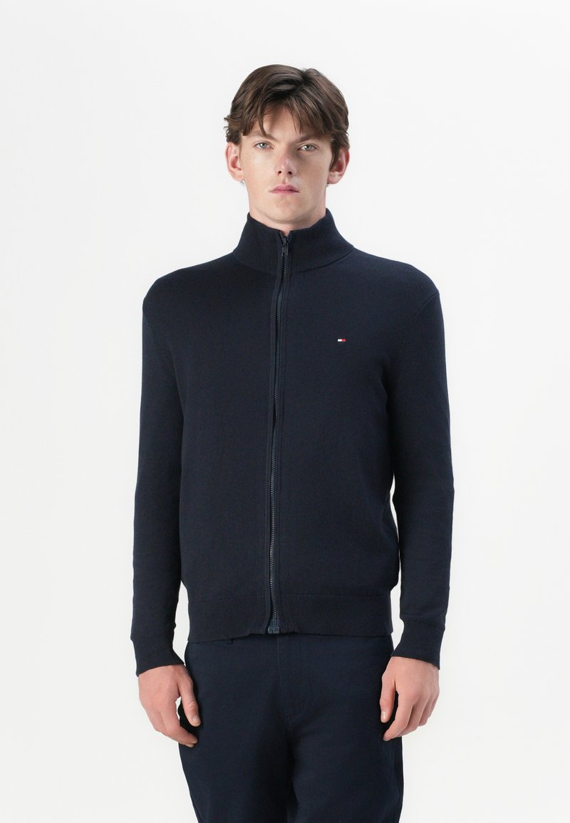 Tume sinine zip-up sviiter kõrge kaelusega, soonikute ja äärtega. Valmistatud pehmest kangast, millel on rindkere küljes väike logo.