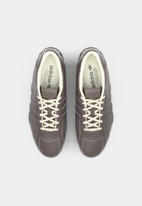 Brown leather sneakers with white laces, three-stripe design, and rubber soles. Interior features branding printed on the insole.