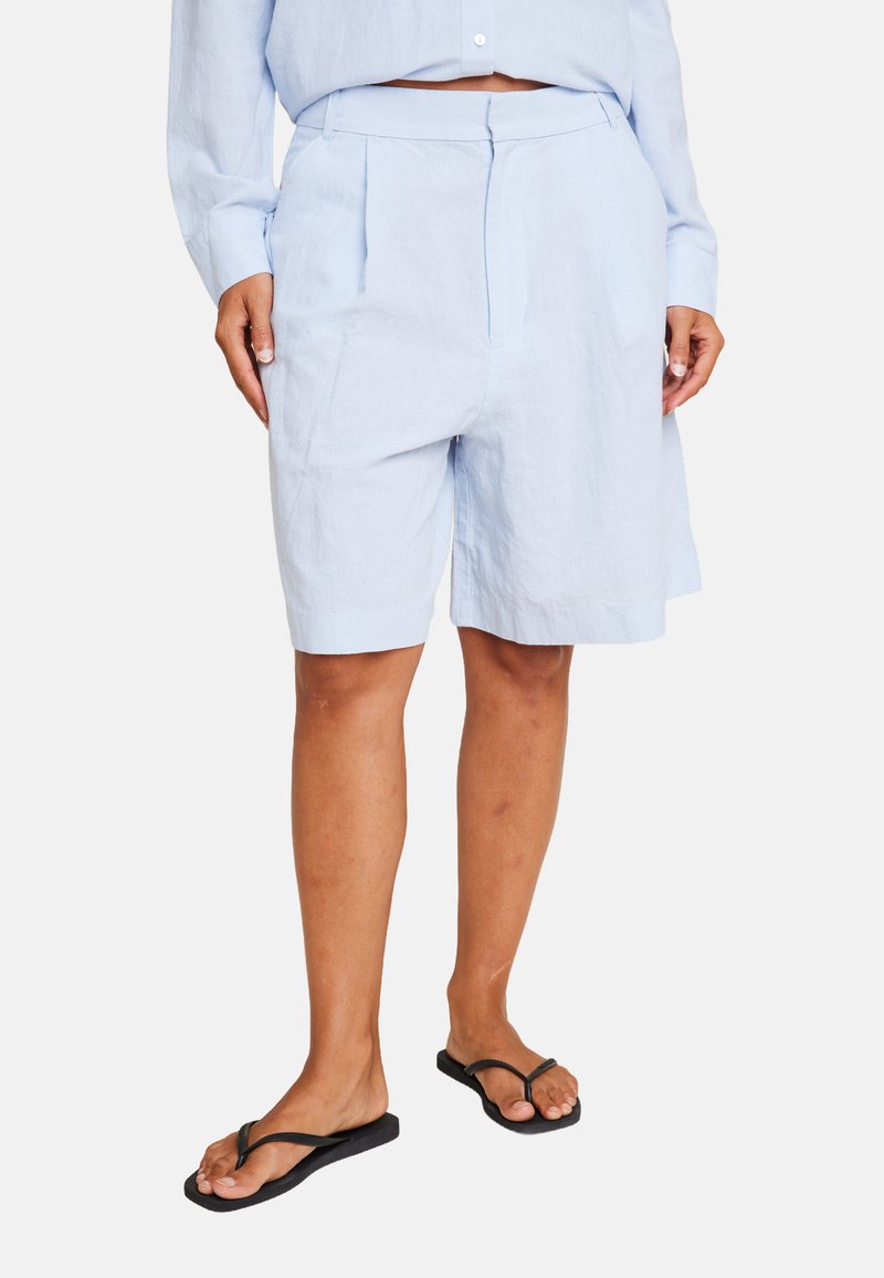 Lys blå linshorts med tilpasset liv, folder foran og en avslappet passform, parret med svarte flip-flops.