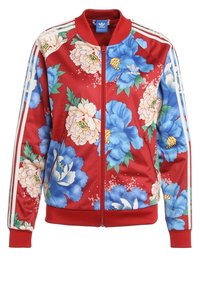 Röd blommig zip-up jacka med stora blå och vita blommor samt gröna accenter. Vita ränder nedanför ärmarna, ribbade manschetter och nederkant.