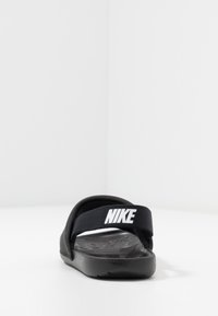 Mustat Nike-sandaalit, joissa on leveä kangasremmi valkoisella logolla, teksturoidut sisäpohjat ja pehmustettu musta ulkopohja.
