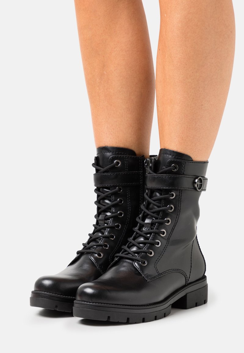 Bottines en cuir noir avec un laçage à l'avant, fermeture éclair sur le côté et détail de sangle avec boucle. Semelle en caoutchouc épaisse avec un motif texturé pour une adhérence optimale.