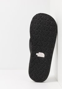 Czarna podeszwa klapka z teksturowanym wzorem bieżnika oraz logo "The North Face". Materiał wydaje się być gumowy i elastyczny.